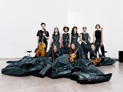 Eine Gruppe Musiker*innen steht und sitzt vor schwarzen Säcken